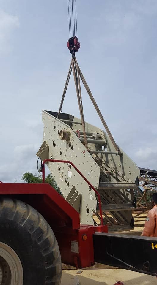 Fabricated steel screen body being lifted by crane above a red trailer
