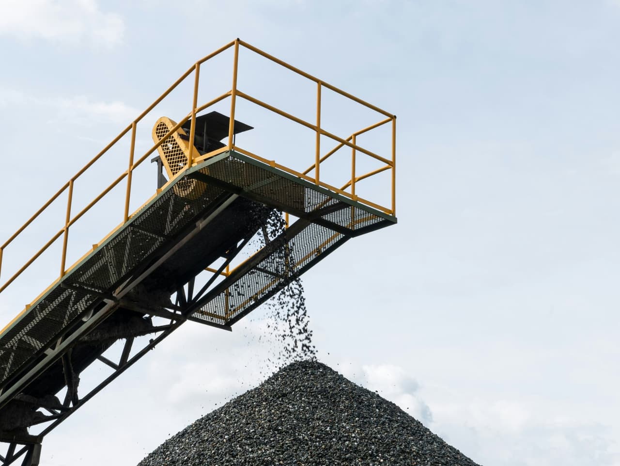Elevated conveyor with a yellow guard-railed platform dropping aggregate onto a stockpile