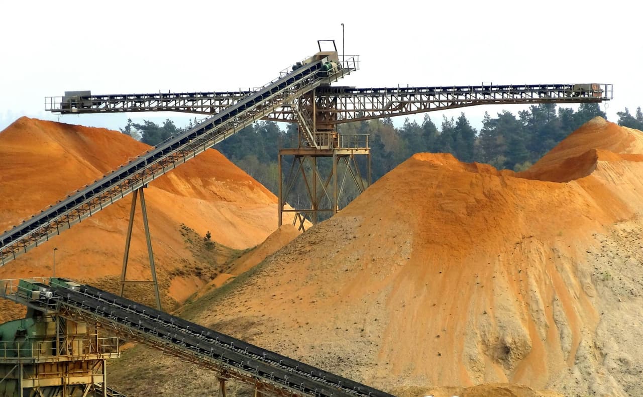 Stacker conveyor and feed conveyors above orange sand stockpiles